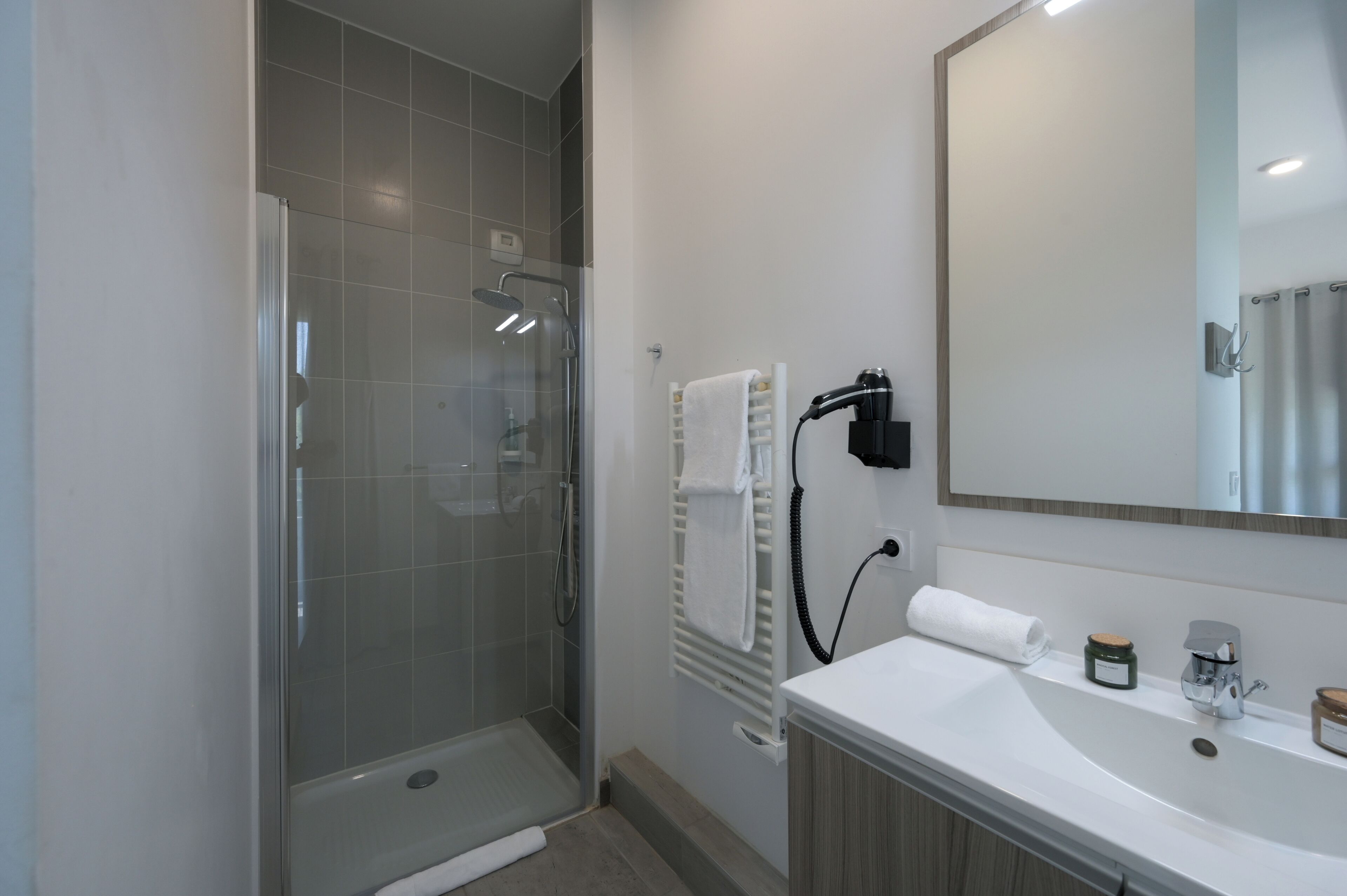 Een moderne badkamer met een douchecabine van glas, een wit wastafeltje met spiegel en een handdoekrek.