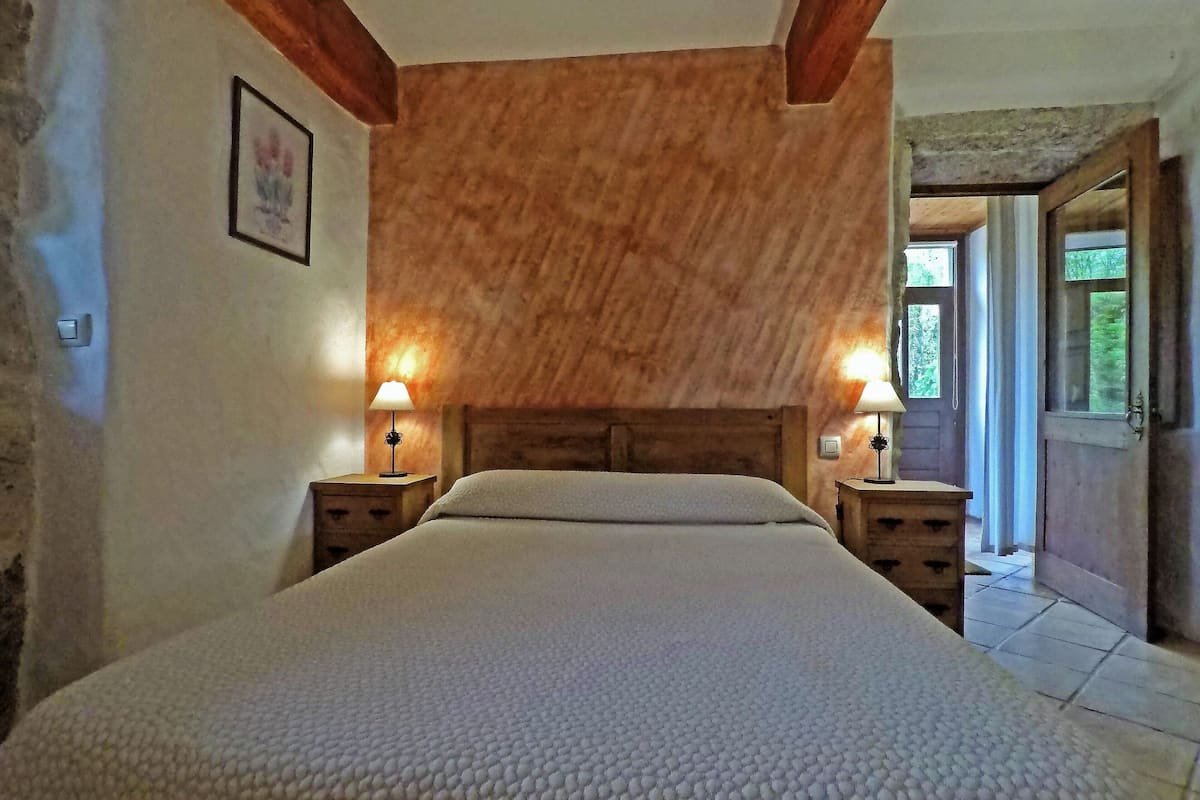 Um quarto com cabeceira de madeira, duas mesas de cabeceira com abajures, uma cama com manta texturizada e um quadro na parede.