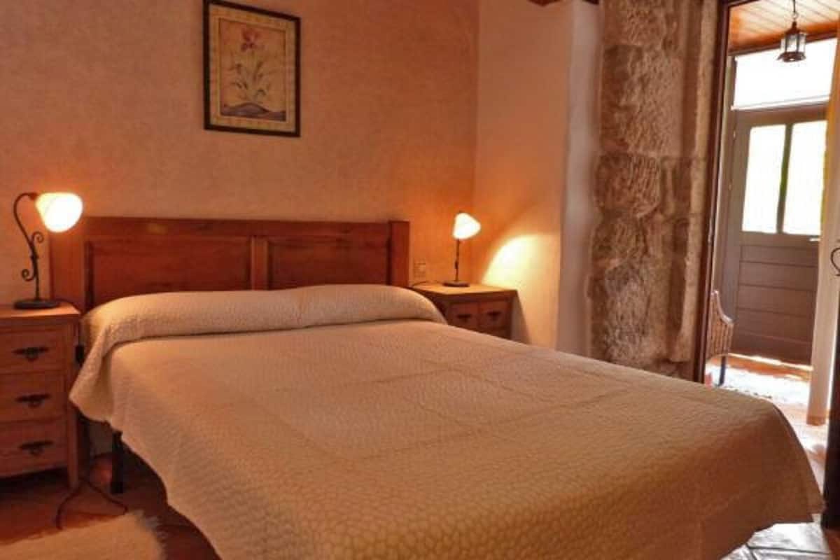 Quarto com cama de madeira, duas luminárias de cabeceira, mesa de cabeceira e parede de pedra.