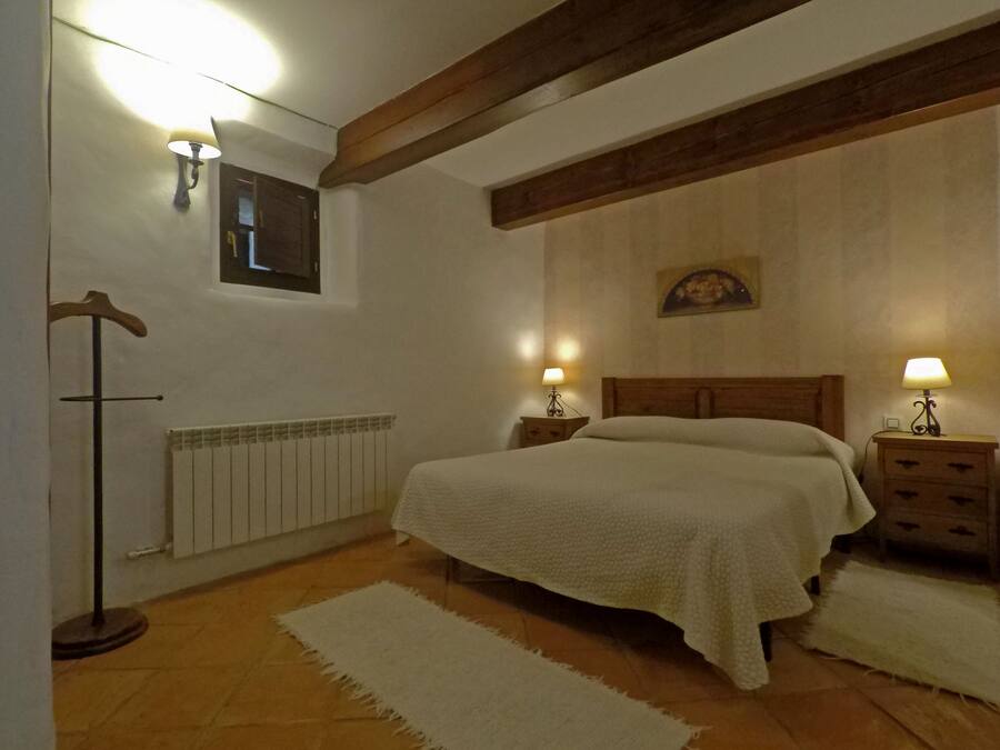 Un dormitorio con una cama grande, vigas de madera, un radiador, dos mesitas de noche con lámparas y un colgante.