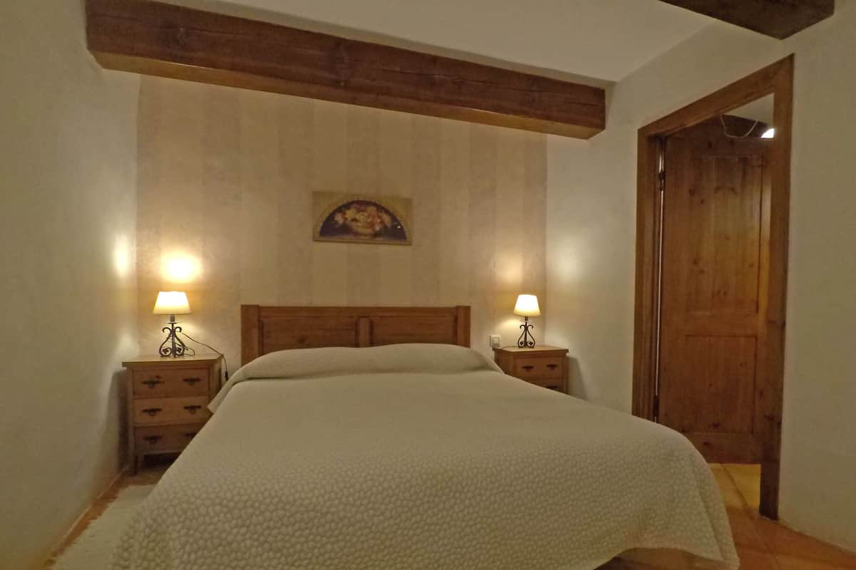 Um quarto com uma cama grande, duas mesas de cabeceira com abajures, um painel de cabeceira de madeira, um quadro na parede e uma porta de madeira.