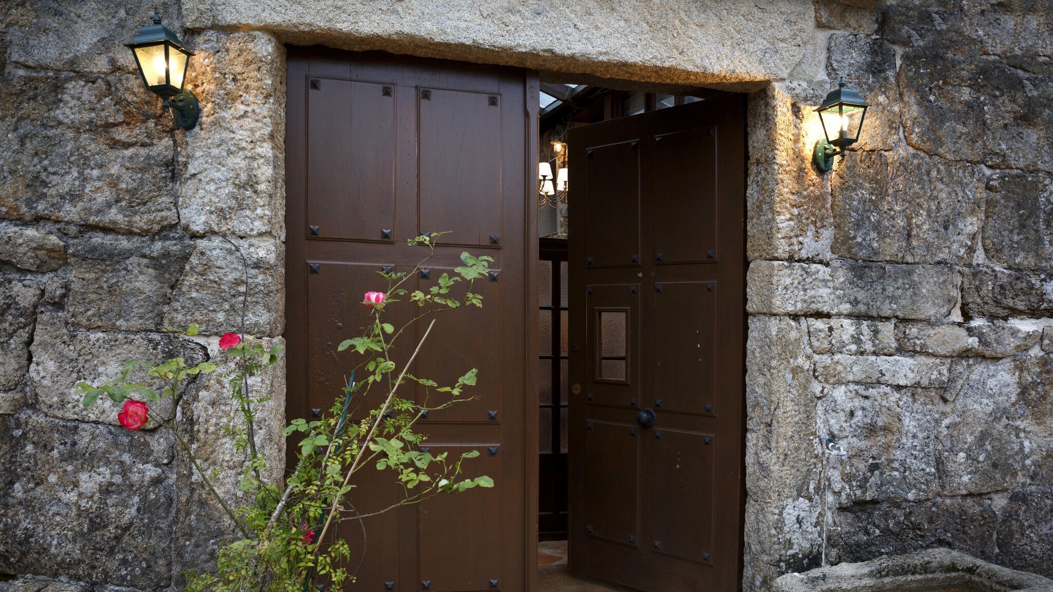 A stone building with a large wooden door and two wall-mounted lanterns.