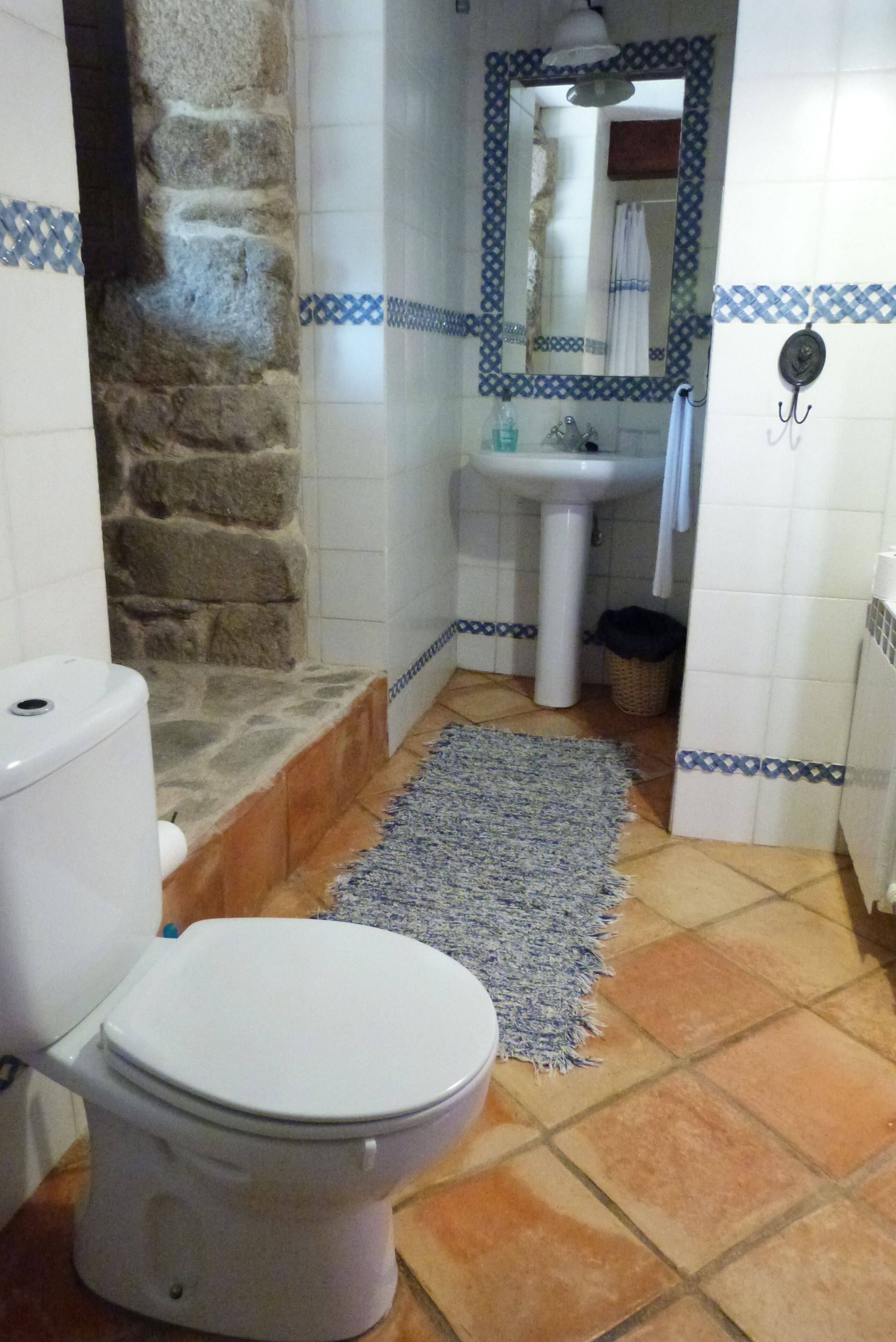 Un baño con inodoro, lavamanos y pared de piedra.