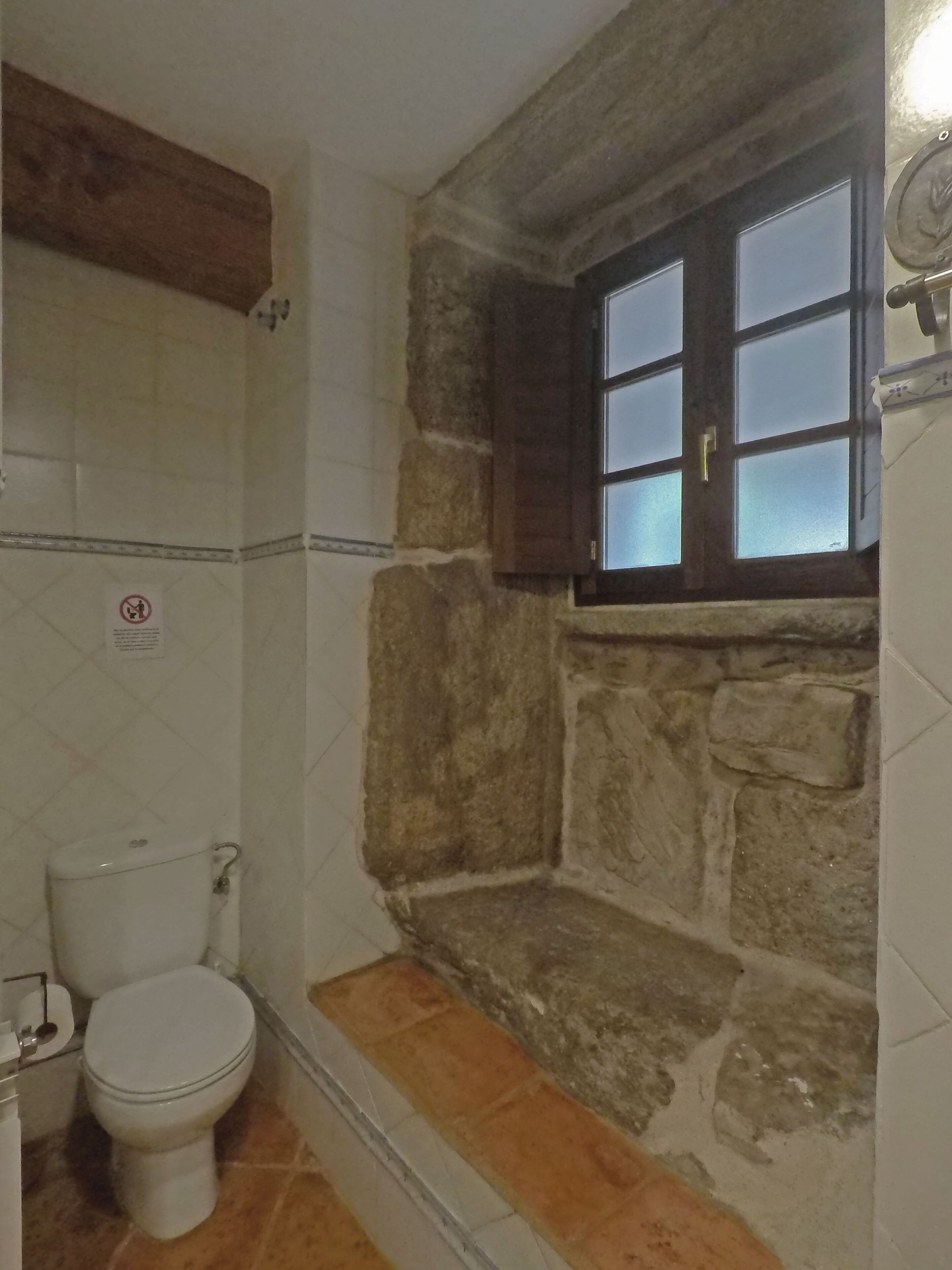 Un baño con pared de piedra, una ventana y un inodoro.