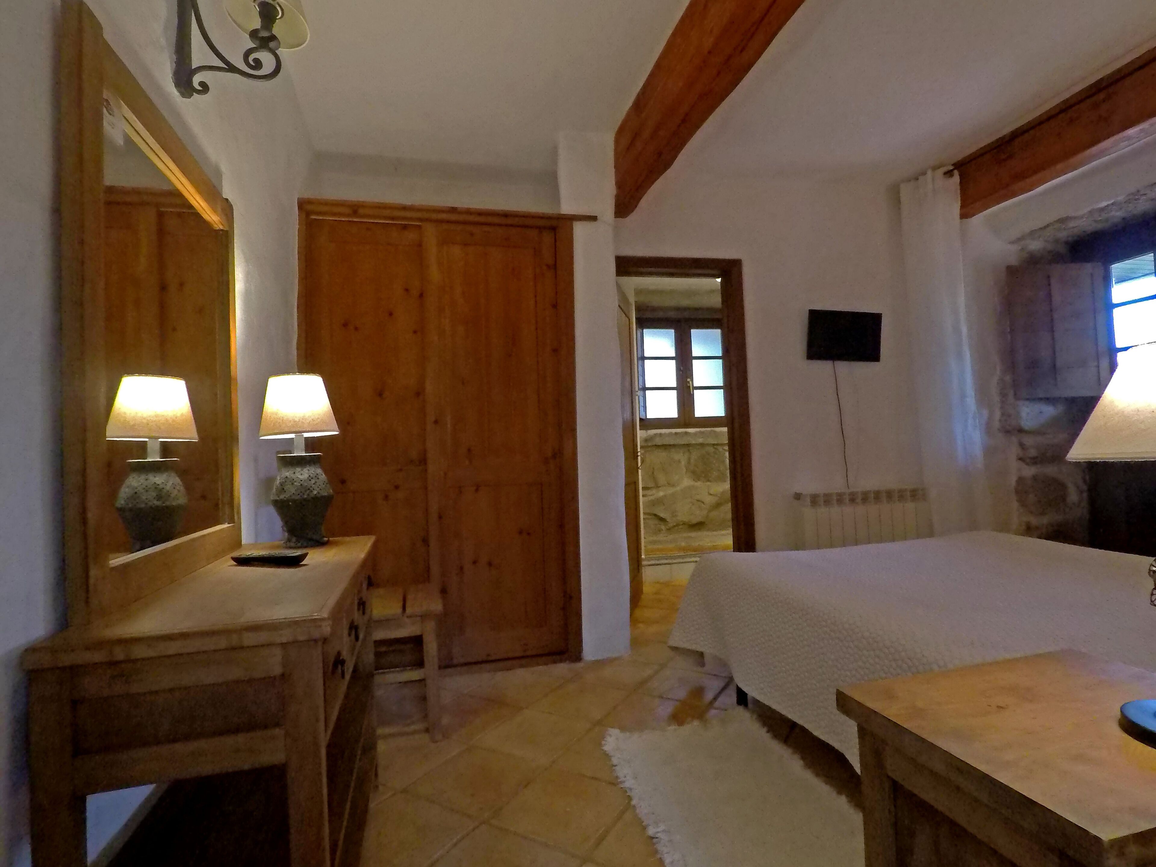 Een slaapkamer met een houten garderobe, een nachtkastje, een spiegel en een lamp.