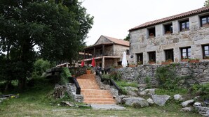 A stone building with a red-tiled roof, a staircase leading to a covered porch, and potted plants on the windowsills. - Lugar Dos Devas (Covelo)