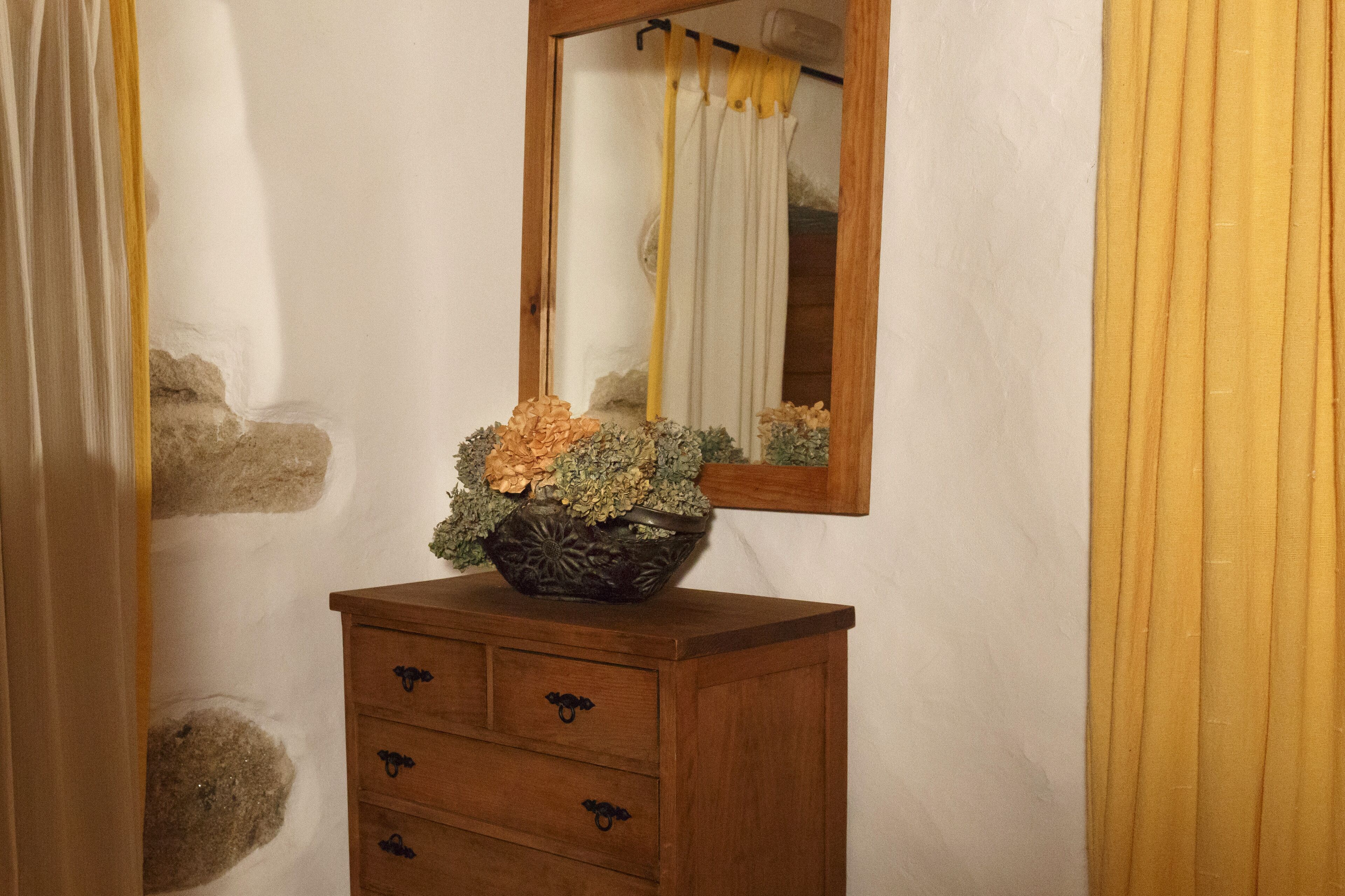 A bathroom with a wooden vanity, a mirror, and a decorative bowl with flowers.