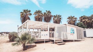 A beachside structure with a covered seating area, palm trees, and a sandy beach. - Halos Casa Resort (Sal)