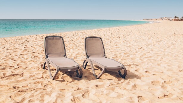 Two empty lounge chairs on a sandy beach with a clear blue sky and calm sea in the background. - Halos Casa Resort (Sal)
