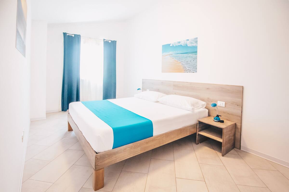 A bedroom with a bed, wooden headboard, bedside table, and a picture of a beach.