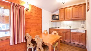 A wooden interior with a dining table and chairs, a microwave, a sink, and wooden cabinets. - Bel Appart proche du Centre, accès Sauna + Piscine (Valfréjus)