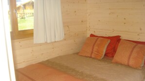 Habitación de una cabaña de madera con cama, almohadas y una ventana con cortinas.