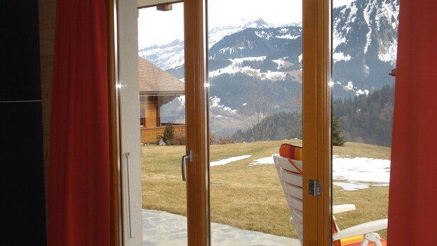 Una habitación con puerta corredera de vidrio que da a un patio con vista a montañas nevadas.