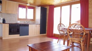 Una cocina con armarios de madera, un refrigerador negro y una zona de comedor con sillas de mimbre y una mesa de madera.