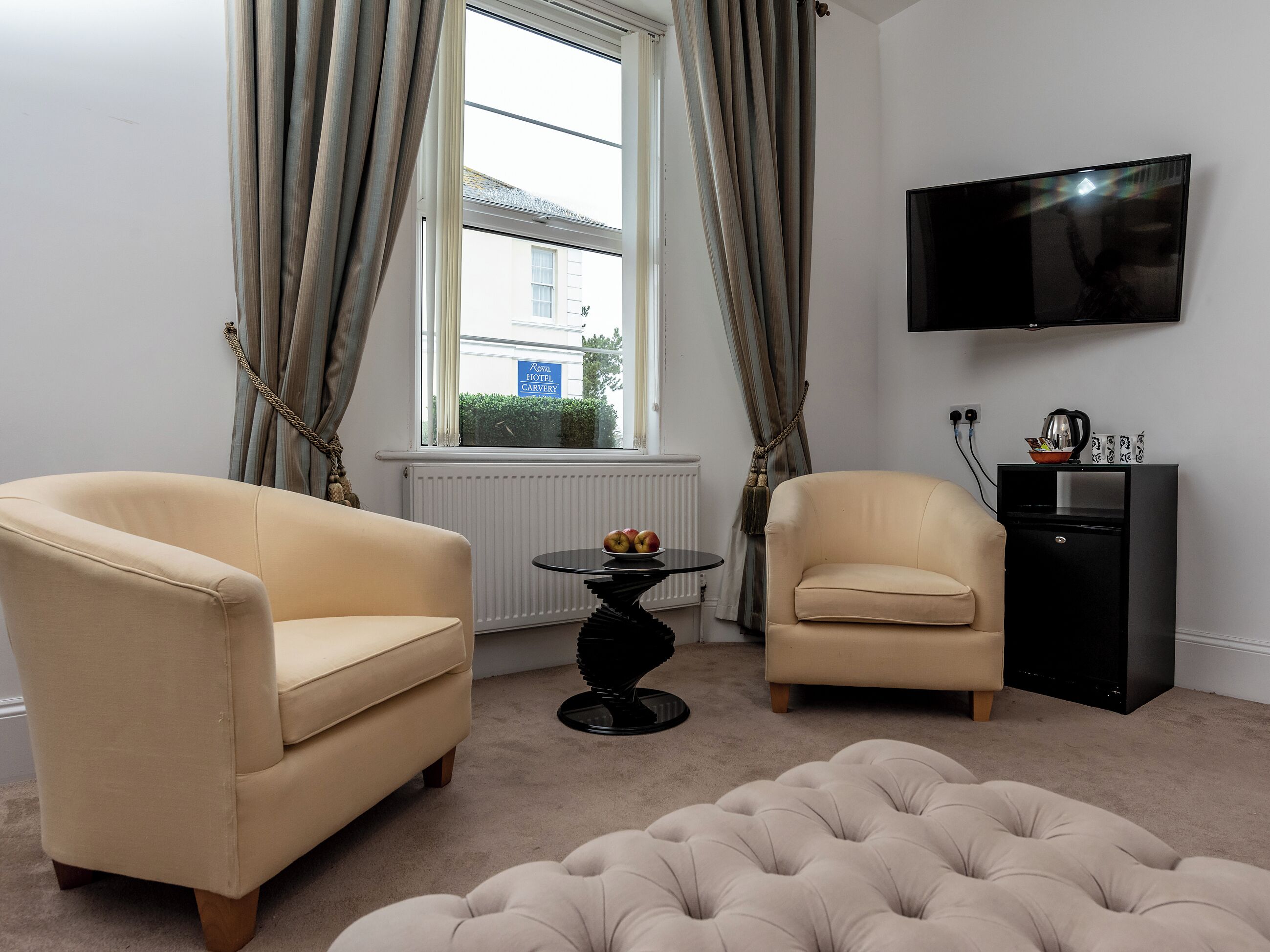 A hotel room with two armchairs, a round table with fruit, a TV, and a black cabinet.