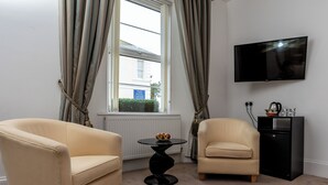 A hotel room with two armchairs, a round table with fruit, a TV, and a black cabinet. - 1 bedroom accommodation in Torquay (Torquay)