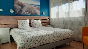 A bedroom with a bed, two nightstands, a lamp, a painting, and a window with sheer curtains.
