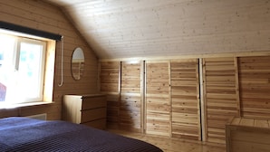 A bedroom with wooden walls, a sloped ceiling, a bed, a dresser, a mirror, and a window. - Comfortable cottage on a beautiful lake (Uro)