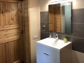 A bathroom with a wooden door, a white sink with a mirror above it, and a green soap dispenser. - Comfortable cottage on a beautiful lake (Uro)
