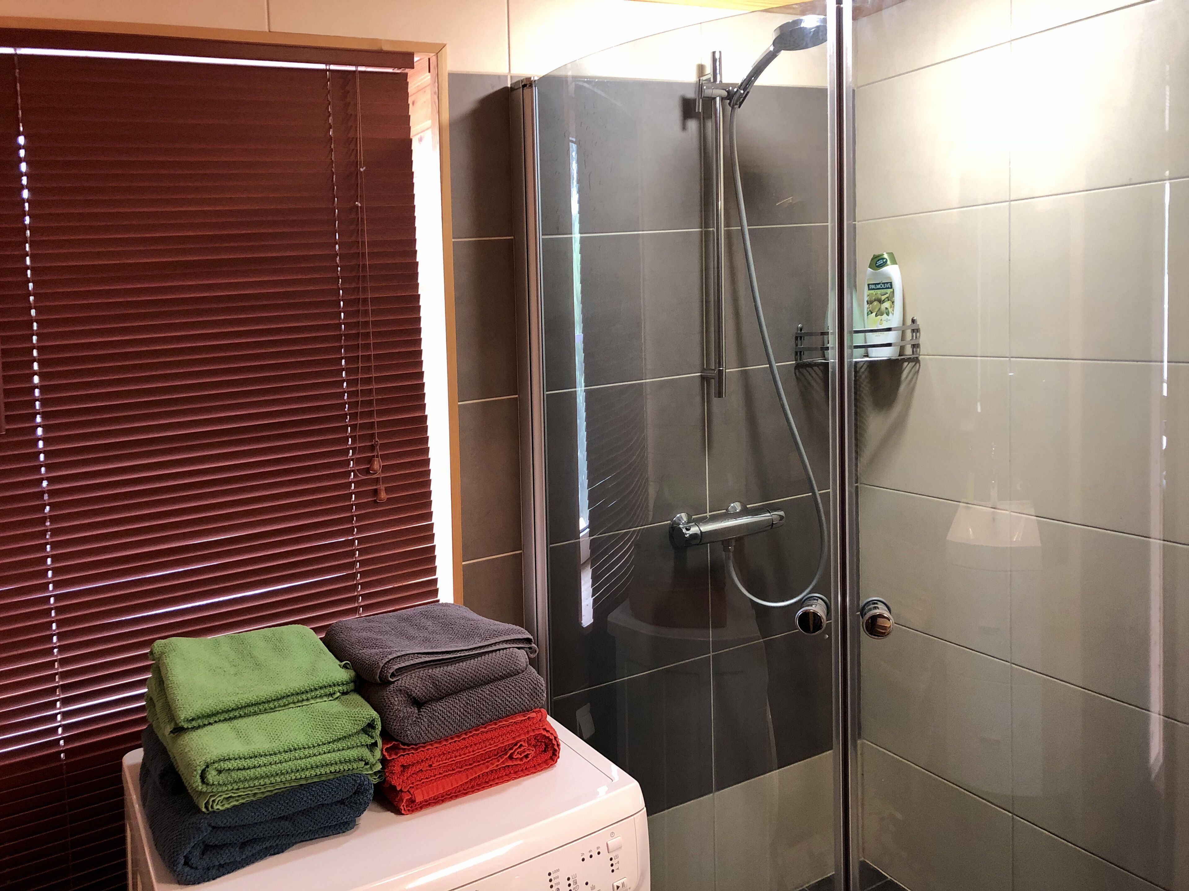 Ein Badezimmer mit einer Duschkabine, einem Stapel gefalteter Handtücher und einer Shampoo-Flasche auf einem Regal.