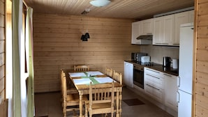 A wooden interior with a dining table, chairs, a kitchen area with white cabinets, a microwave, a kettle, and a refrigerator. - Comfortable cottage on a beautiful lake (Uro)