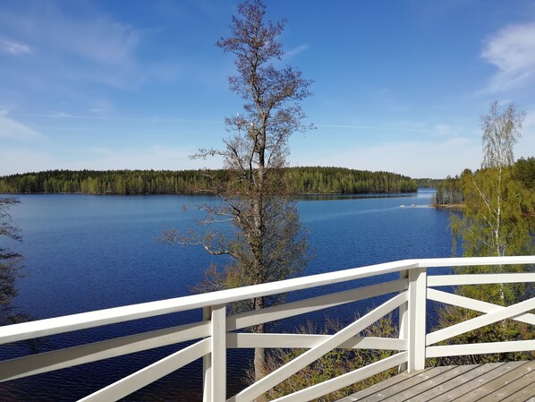 A wooden deck with white railings overlooking a calm lake surrounded by dense forest. - Comfortable cottage on a beautiful lake (Uro)