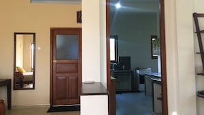 A hallway with a wooden door, a mirror, and a view into a kitchen area with a stove and cabinets. - Paddy House Villa (Ranna)