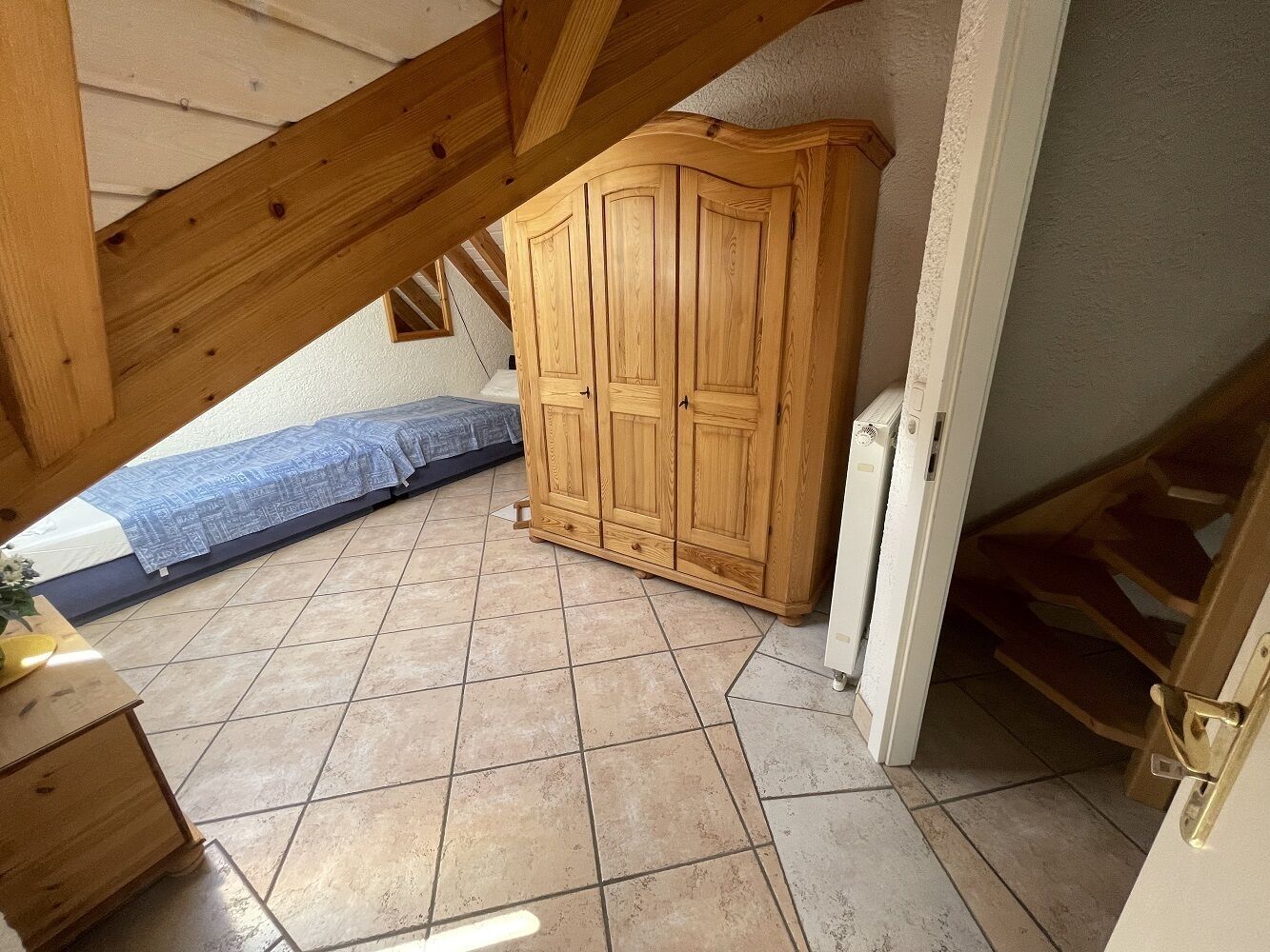 Ein Zimmer mit Holzschrank, Bett mit blauer Bettdecke und Fliesenboden.
