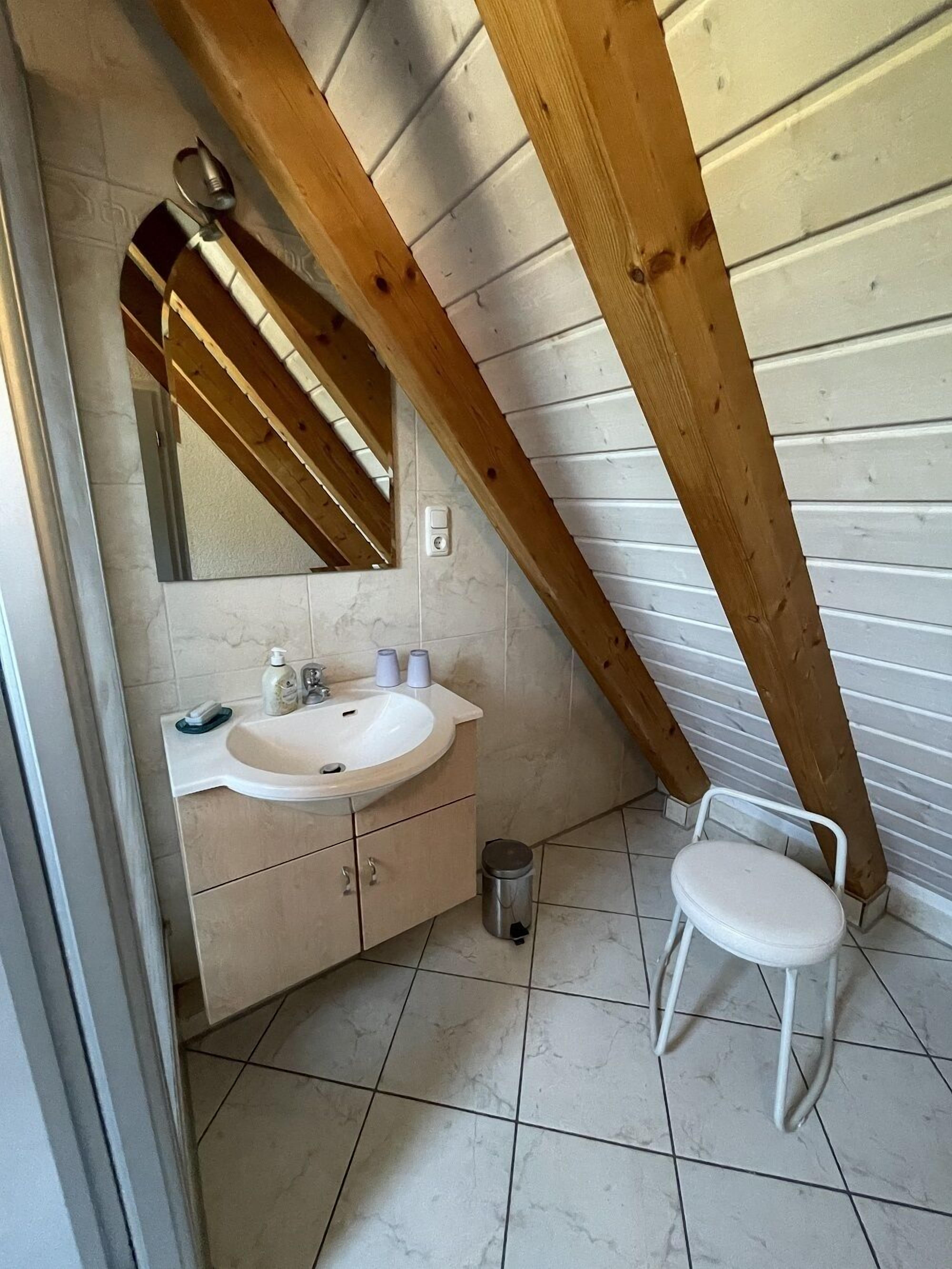 A small bathroom with a white sink, mirror, and a white chair.