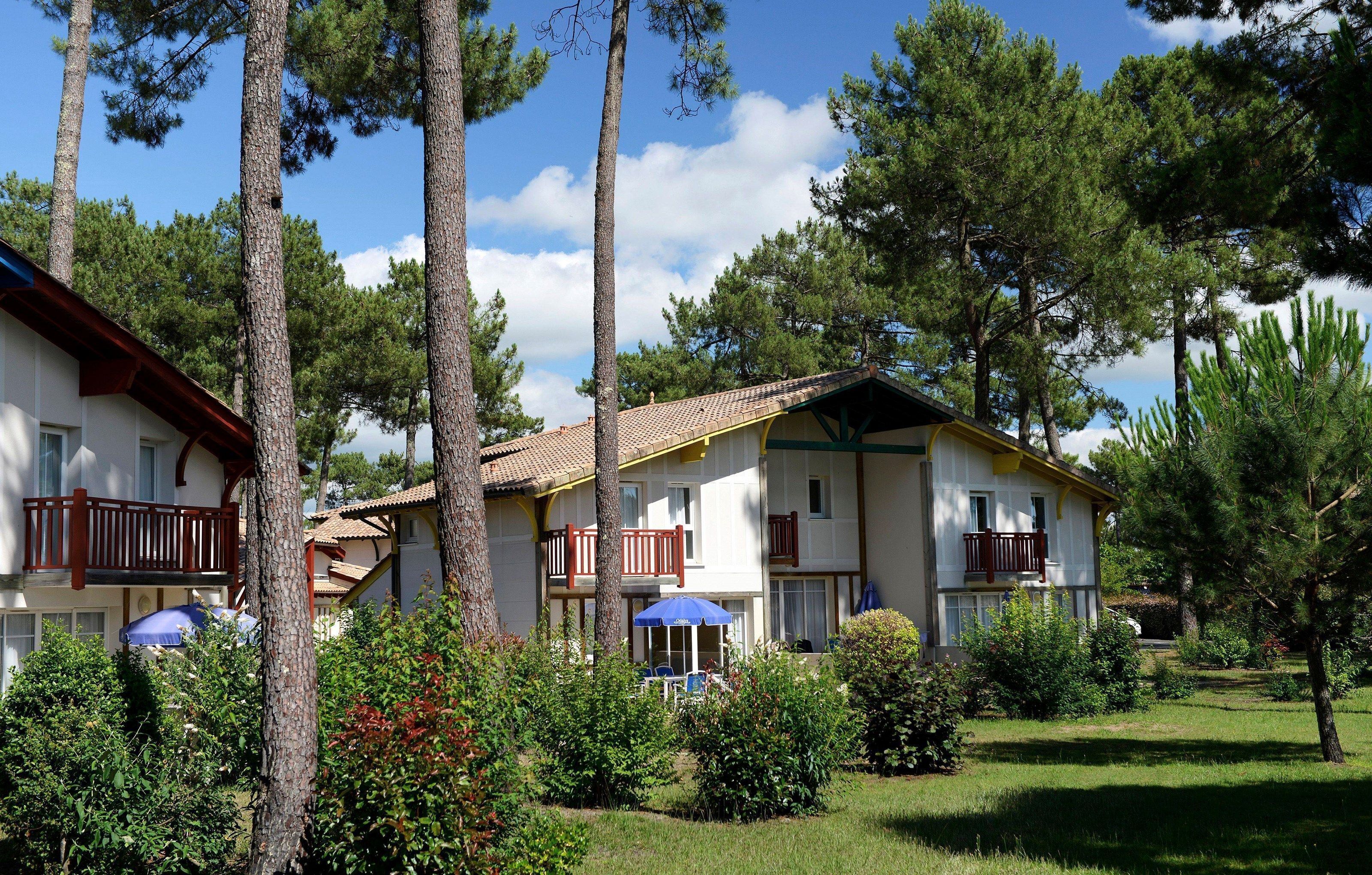 Un immeuble à deux étages doté de balcons, entouré d’arbres et de verdure.