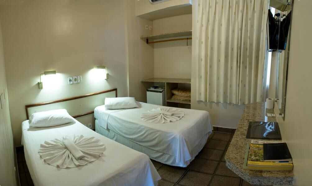 A hotel room with two beds, a small desk, a wardrobe, and a bathroom.