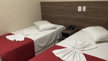 Two single beds with red quilts and white pillows, a wooden headboard, a bedside table with a phone, and two wall sockets.