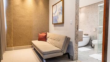 A modern bathroom with a beige sofa, a framed abstract painting, and a glass shower enclosure.