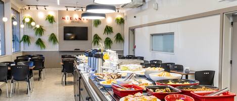 A buffet area with various food options, black chairs, and a wall-mounted TV.