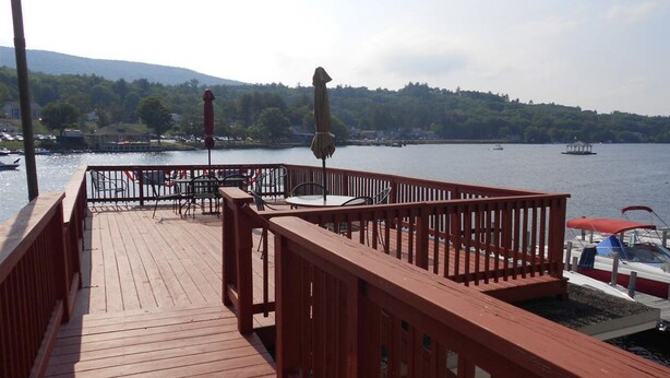 A wooden deck with outdoor seating and a view of a lake with boats and a gazebo in the distance. - Cozy cottage get-away at Lake Winnipesaukee with swim access off dock (Alton)