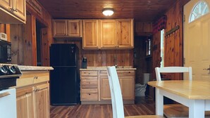 A kitchen with wooden cabinets, a black refrigerator, a microwave, and a dining table with chairs. - Cozy cottage get-away at Lake Winnipesaukee with swim access off dock (Alton)