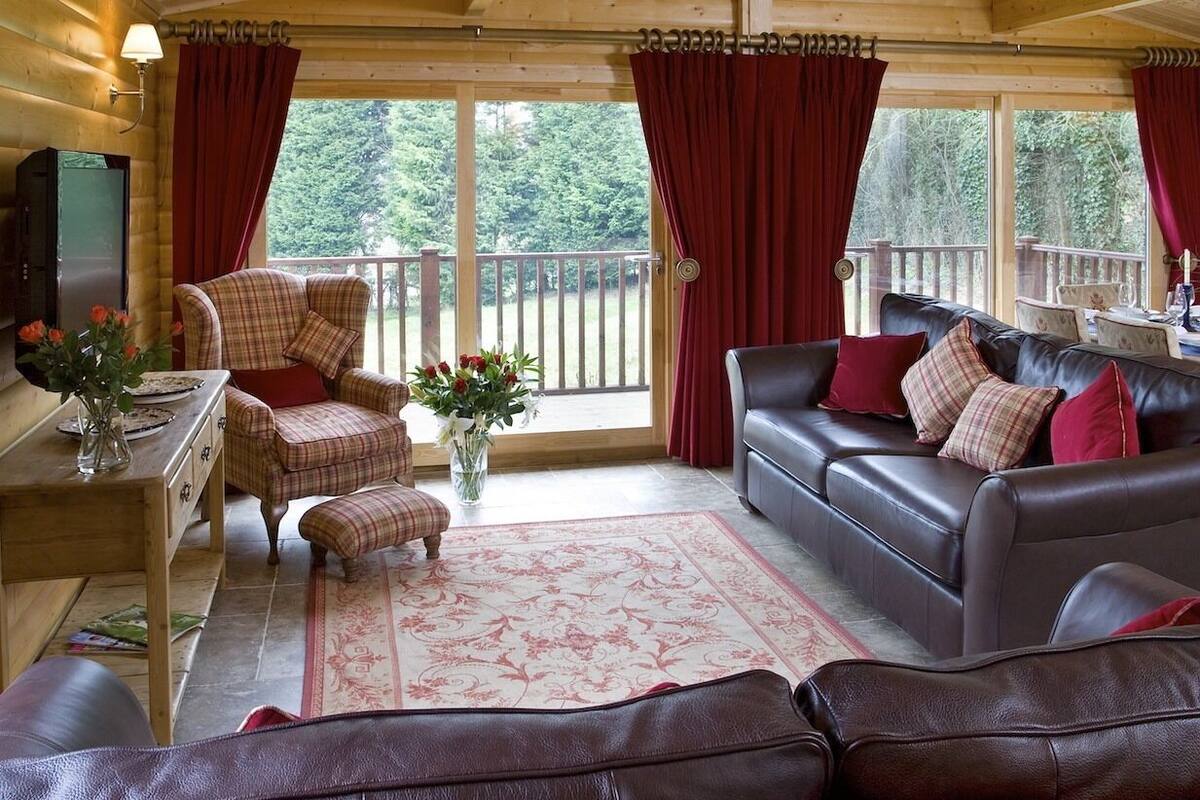 A cozy cabin interior with a wooden interior, a sofa, a chair, a small table with a vase of flowers, and a television.
