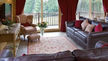 A cozy cabin interior with a wooden interior, a sofa, a chair, a small table with a vase of flowers, and a television.