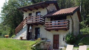 A two-story stone building with a balcony, a wooden staircase, and a door. There are two lounge chairs in the front yard.