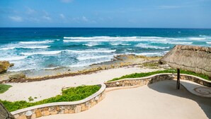 Une plage avec une structure recouverte de chaume, un mur de pierre et une vue sur l’océan.