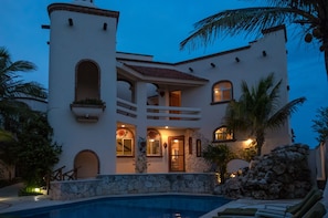 A white building with a pool, stone walls, and palm trees.