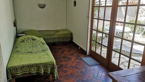 A room with two beds, a wooden table, and a view of the outside through a glass door.