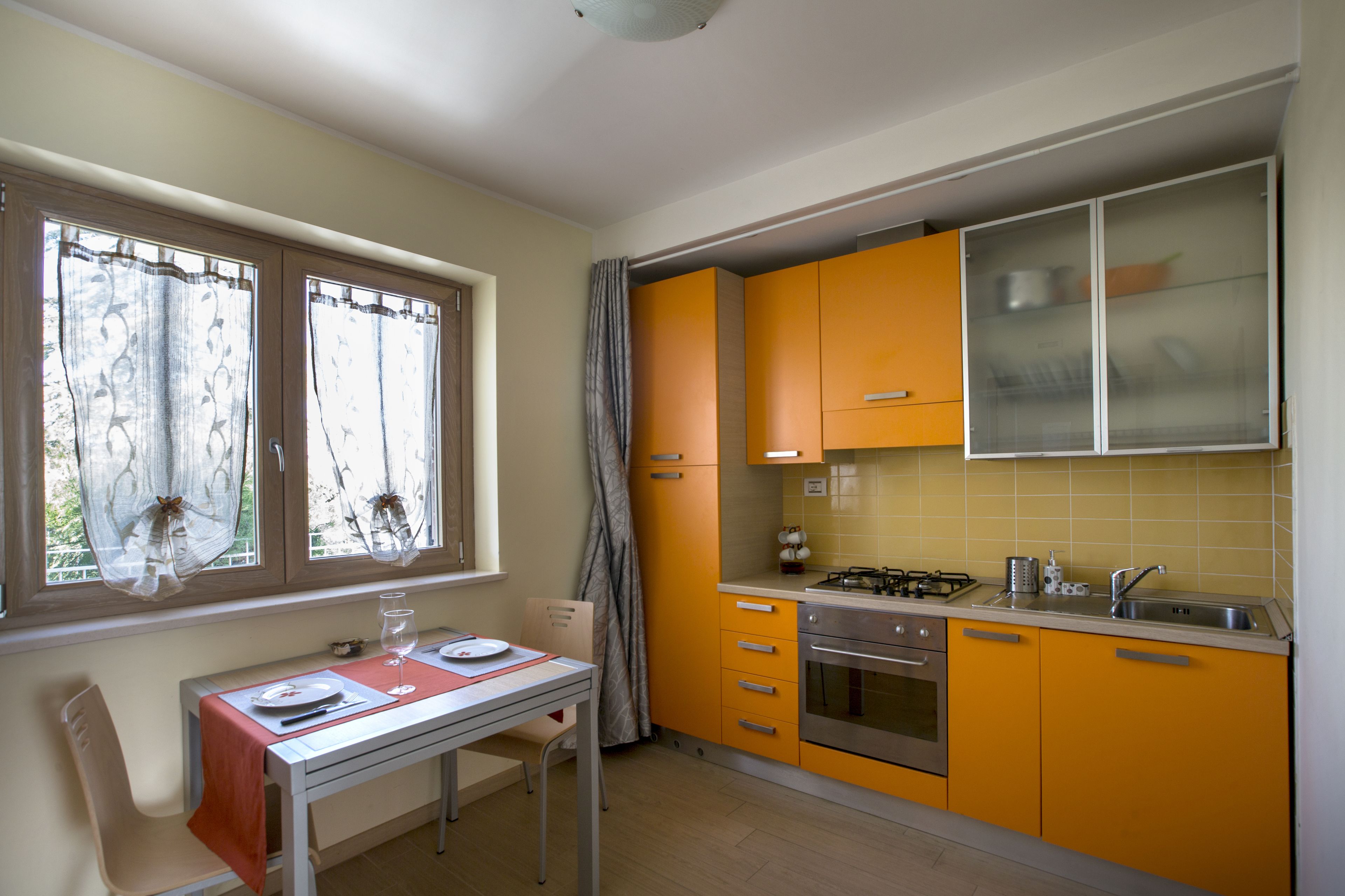 Een compacte keuken met gele kastjes, een eettafel met stoelen en een raam met gordijnen.