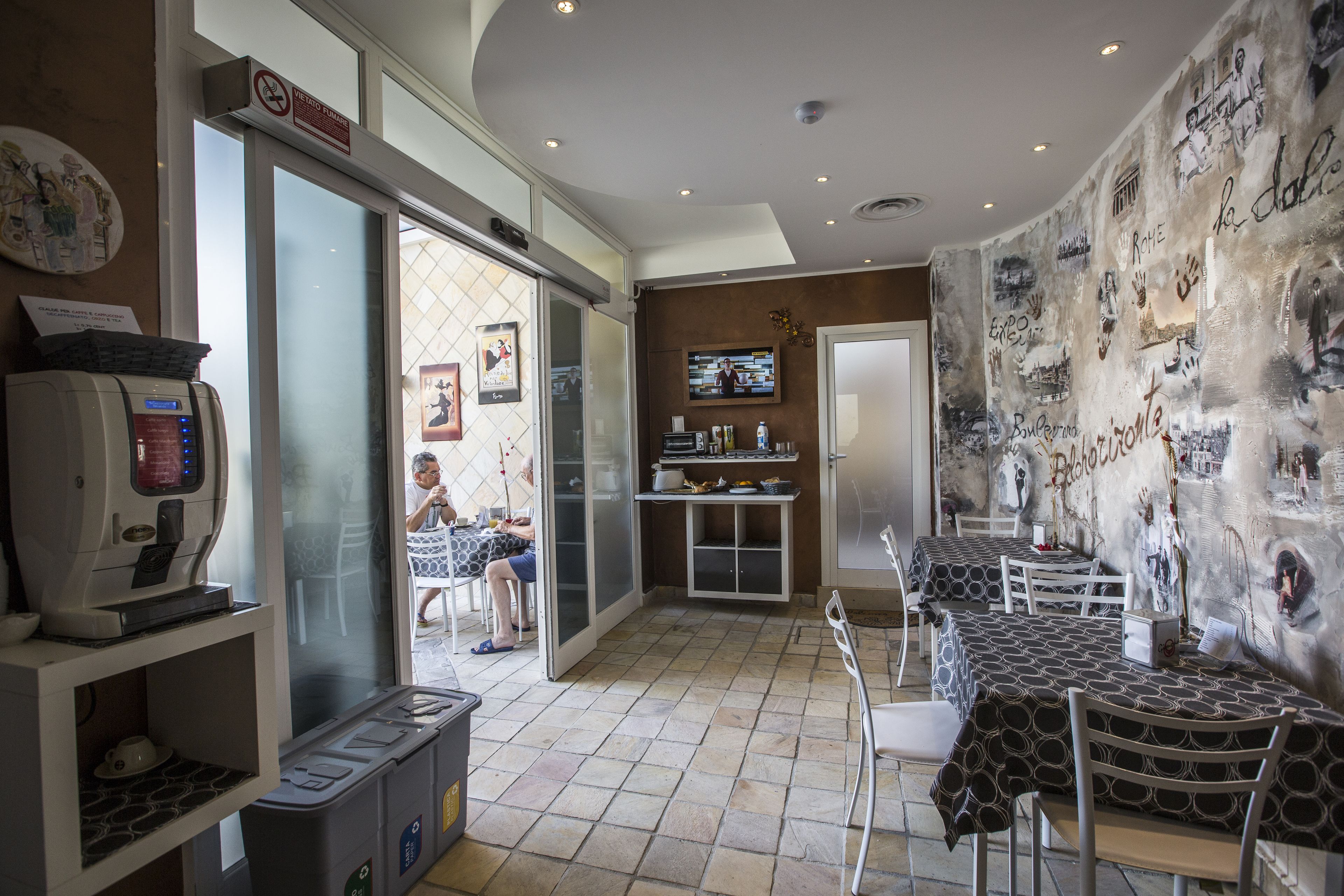 A restaurant with a coffee machine, tables, chairs, and a wall with artwork.