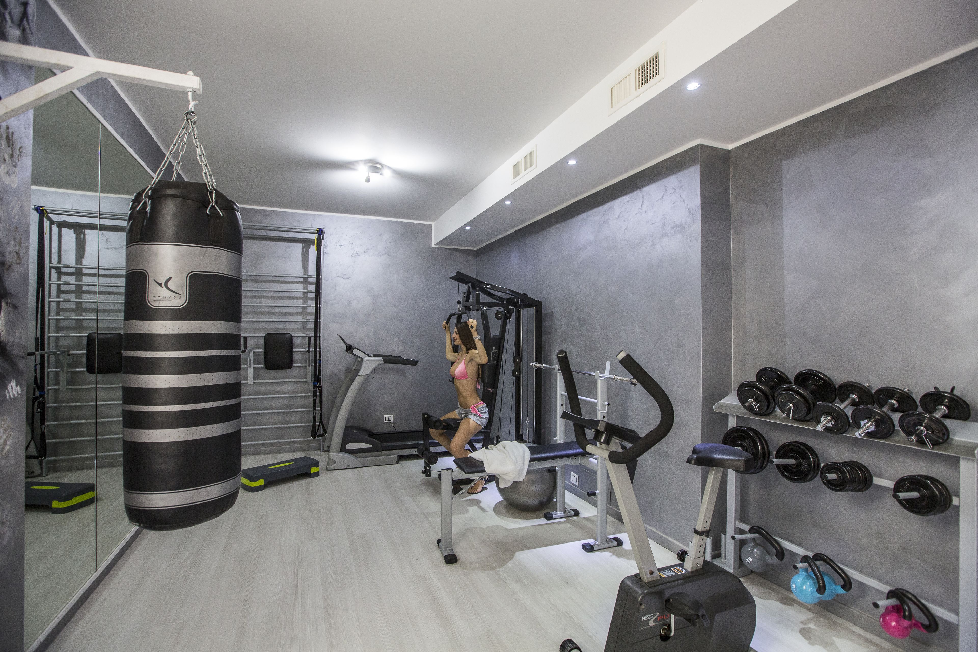 A gym with a punching bag, exercise equipment, and a wall of dumbbells.