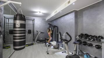 A gym with a punching bag, exercise equipment, and a wall of dumbbells.