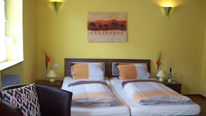 A double bed with a wooden headboard, two bedside tables with lamps, a chair with a patterned cushion, and a wall painting of elephants. - Pension  Zum Stern (Freudenberg)