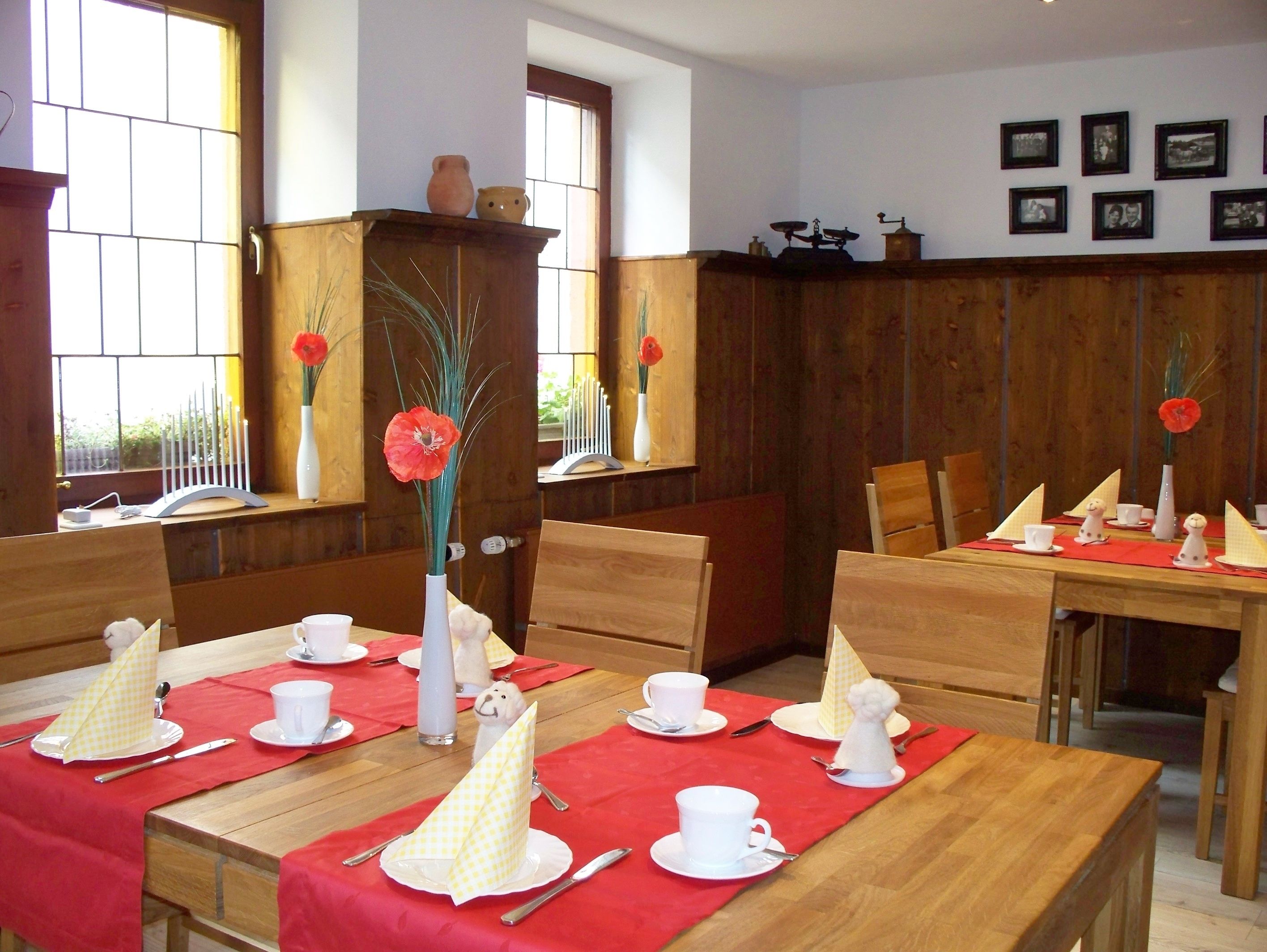 A dining area with wooden tables set for a meal, featuring white tableware and red tablecloths.