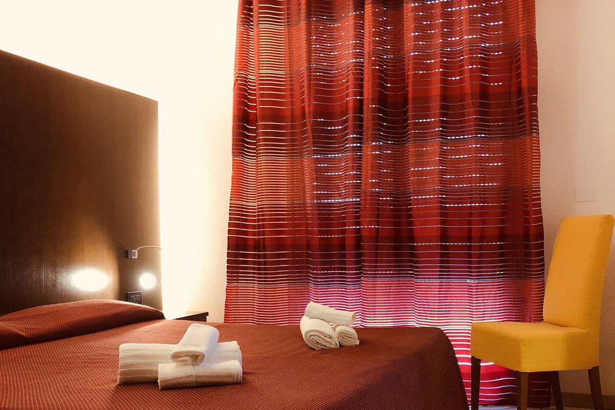 Una habitación de hotel con una cama, una silla y una cortina roja.