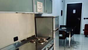 Una cocina moderna con electrodomésticos de acero inoxidable, un comedor con mesa y sillas, y una puerta negra al fondo.